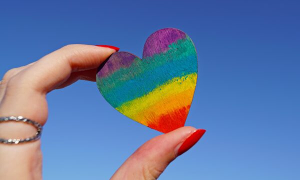 Hand holding small heart painted rainbow colors