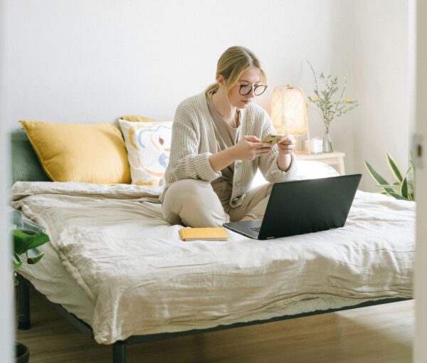 Woman working from home on her bed with laptop and phone
